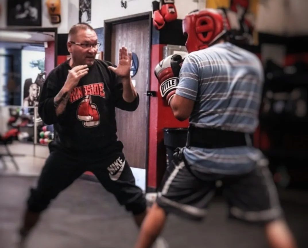 Two people in a boxing stance, training in a gym with red gloves and headgear